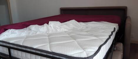 A single bed with a white mattress and a dark headboard in a room with wooden flooring.
