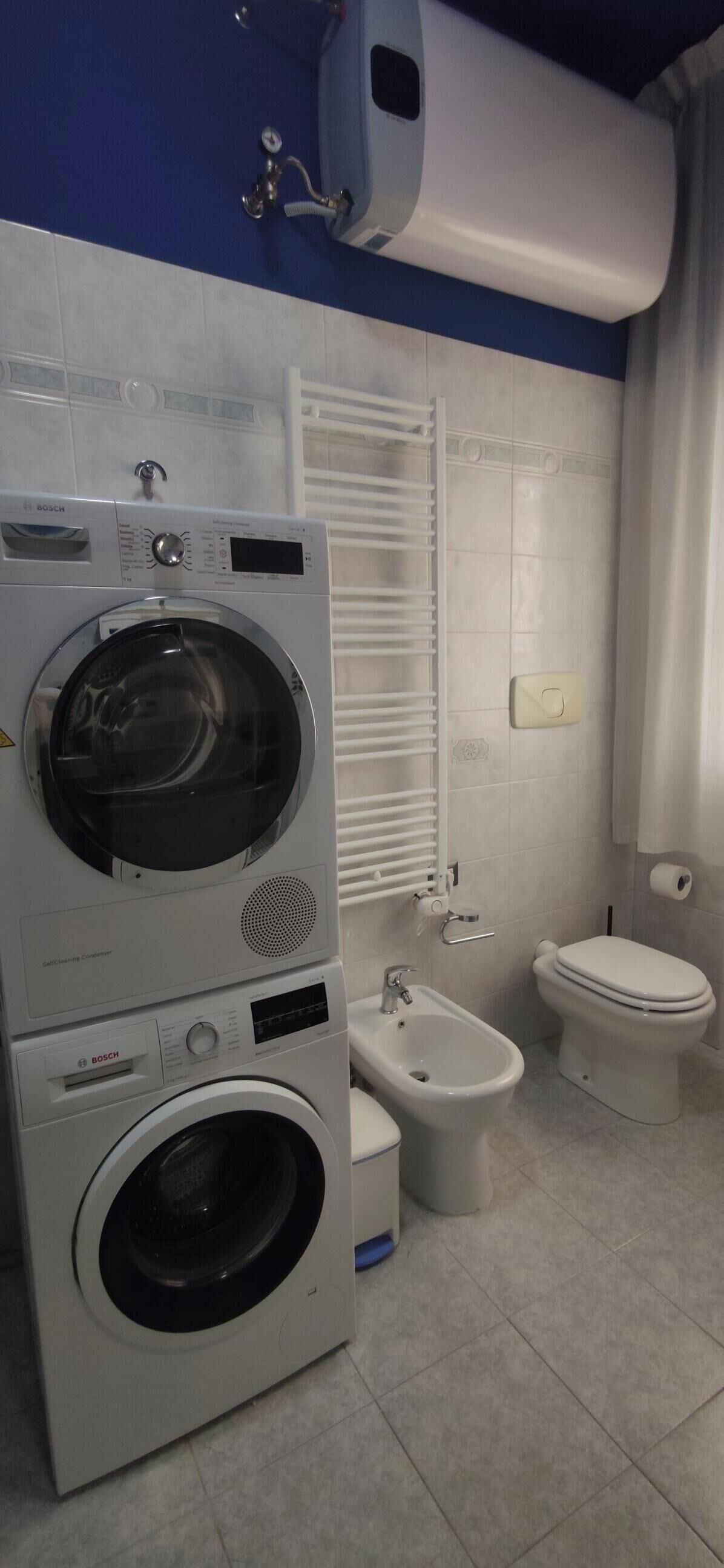 Une buanderie équipée de machines à laver superposées, d’un bidet et de toilettes.
