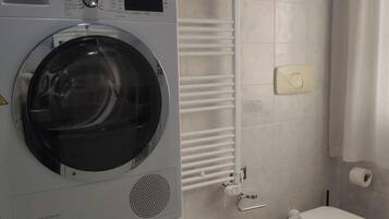 Une buanderie équipée de machines à laver superposées, d’un bidet et de toilettes.