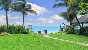 A pathway leading to a beach with two chairs and a table, surrounded by lush greenery and palm trees. - Oceanfront Villa With Privet Beach Access ! (Fort Lauderdale)