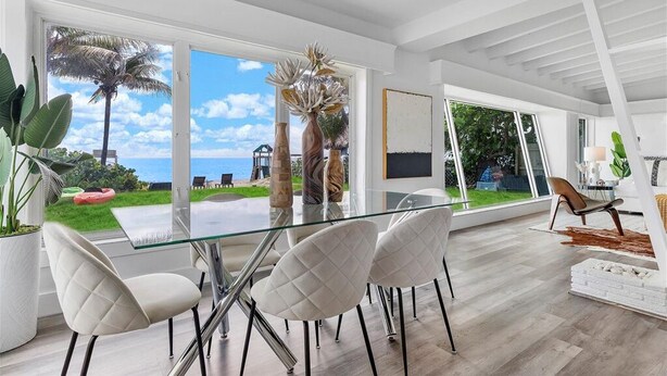 A modern dining area with a glass table and white chairs, large windows offering a view of the sea and palm trees, and a minimalist interior design. - Oceanfront Villa With Privet Beach Access ! (Fort Lauderdale)