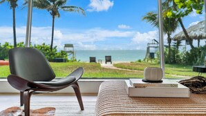A room with a view of the beach, a chair, a book, and a decorative item on a table. - Oceanfront Villa With Privet Beach Access ! (Fort Lauderdale)