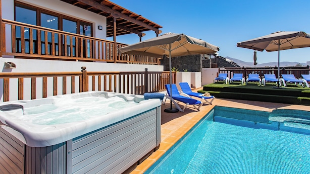Ein Poolbereich mit Whirlpool, Liegestühlen und Sonnenschirmen.