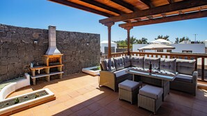 Eine Terrasse im Freien mit einer Steinmauer, einem Backofen aus Ziegeln, Korbmöbeln und einem Glastisch.