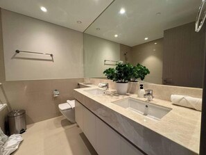 Une salle de bain moderne avec un grand miroir, deux lavabos, des toilettes et une poubelle.