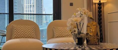 A modern living room with two white armchairs, a round black and white striped table, and a vase with white orchids.