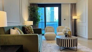 A modern living room with a green sofa, two armchairs, a striped coffee table, and a large window with a city view.