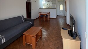 Una sala de estar con sofá, una mesa de centro de madera, un mueble para televisión y un comedor con mesa y sillas.