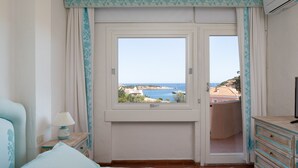 Une chambre à coucher avec un grand lit, une table de chevet, une commode et une fenêtre donnant sur la mer et les bâtiments.