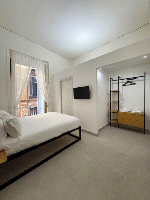 A bedroom with a bed, a TV, a closet with a clothing rack, and a balcony view. - Nabab-Napoli Bed and Breakfast (Naples)