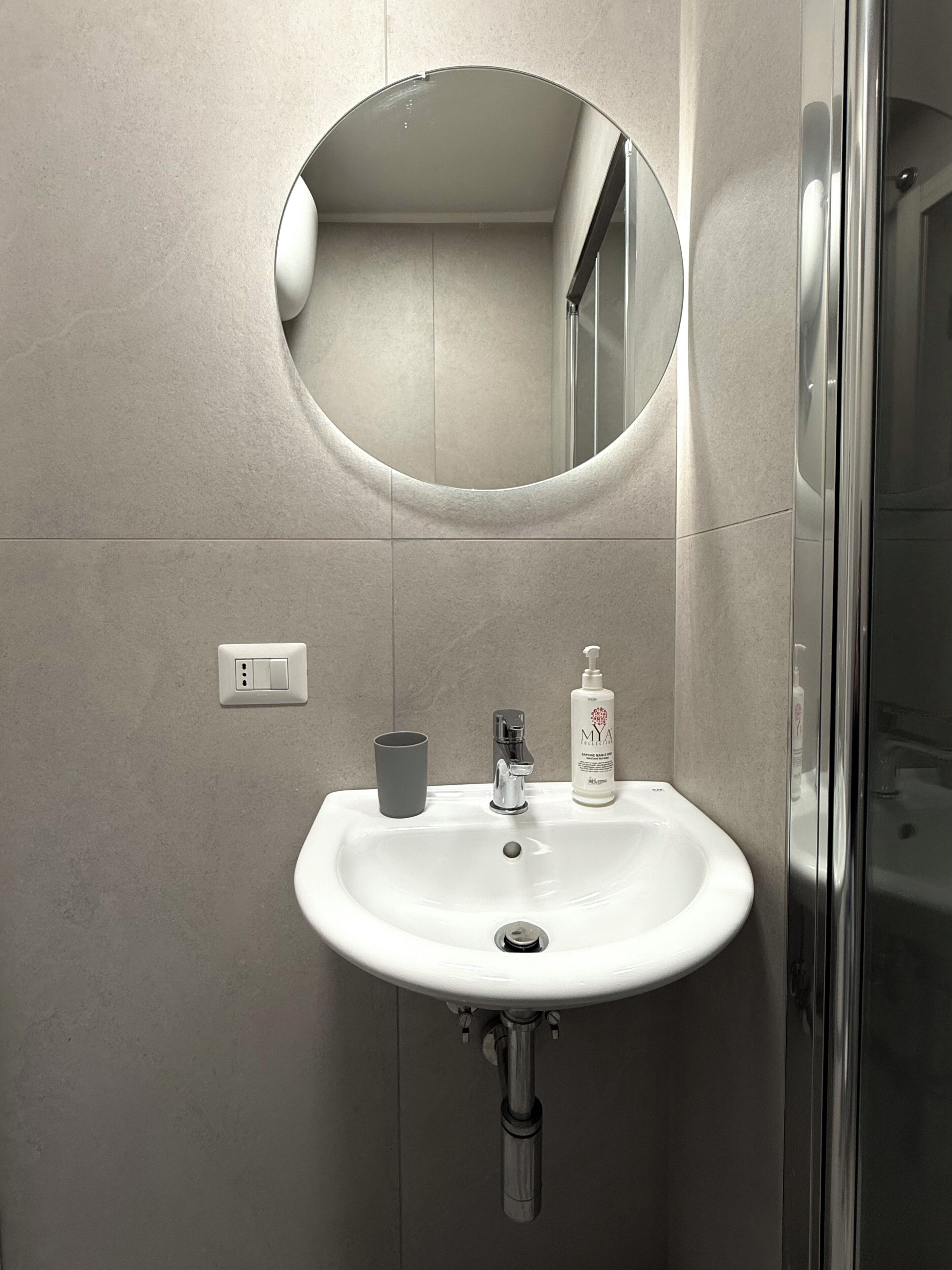 A bathroom with a white sink, a mirror, a faucet, and a bottle of hand soap.