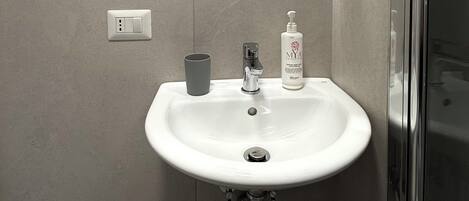 A bathroom with a white sink, a mirror, a faucet, and a bottle of hand soap.
