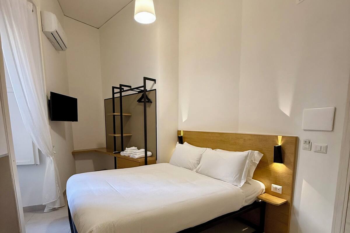 A modern hotel room with a bed, bedside table, lamp, and a TV mounted on the wall.