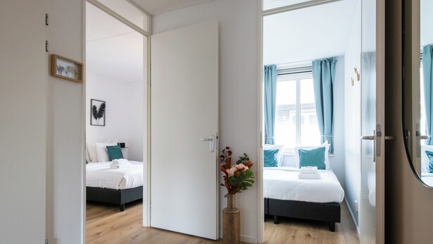 Un dormitorio moderno con dos camas, piso de madera y un jarrón con flores.
