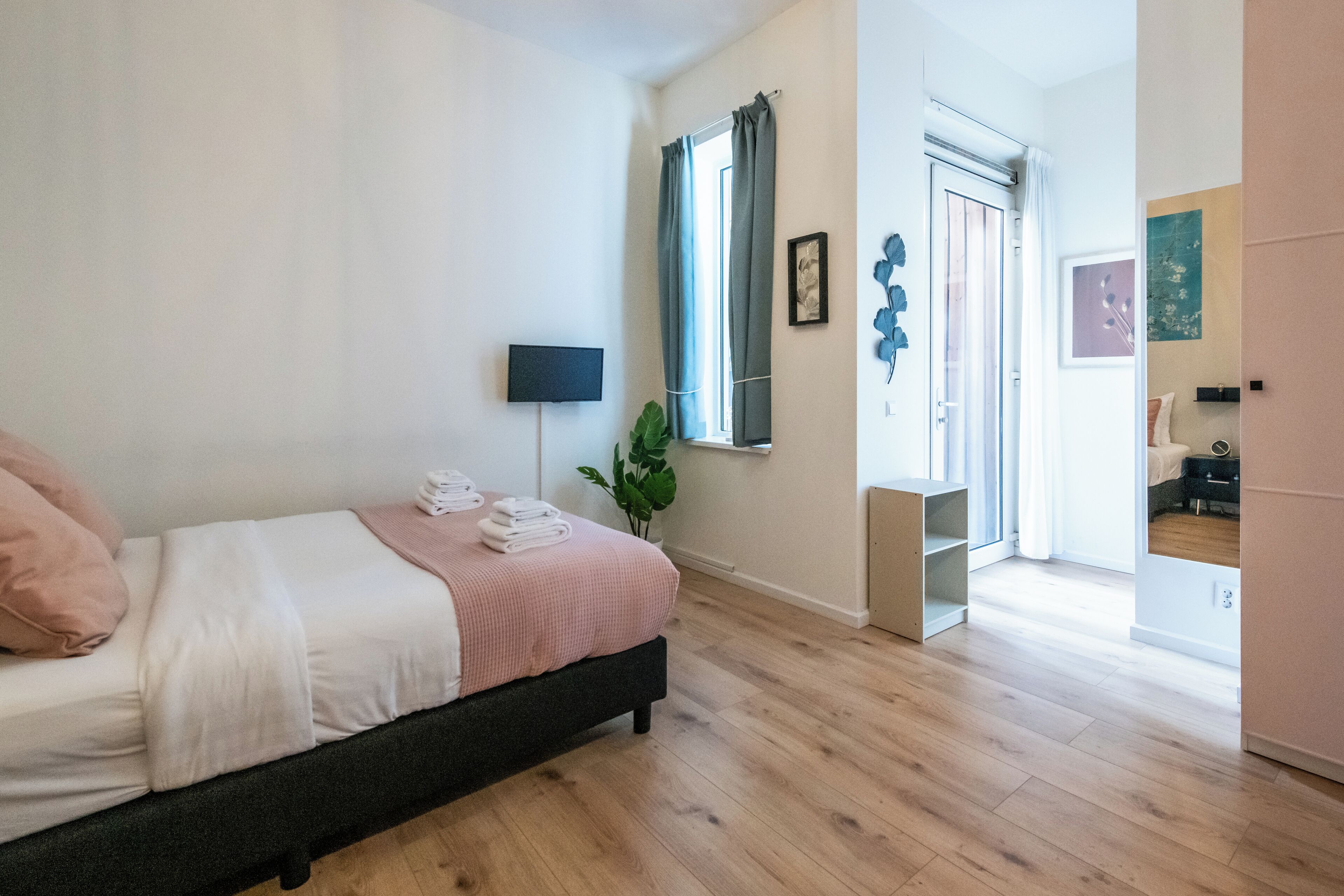 Une chambre à coucher avec un lit, une table de chevet, une plante en pot et une fenêtre avec des rideaux.