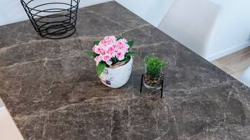 A marble table with a white vase of pink flowers, a small potted plant, and a wire basket.