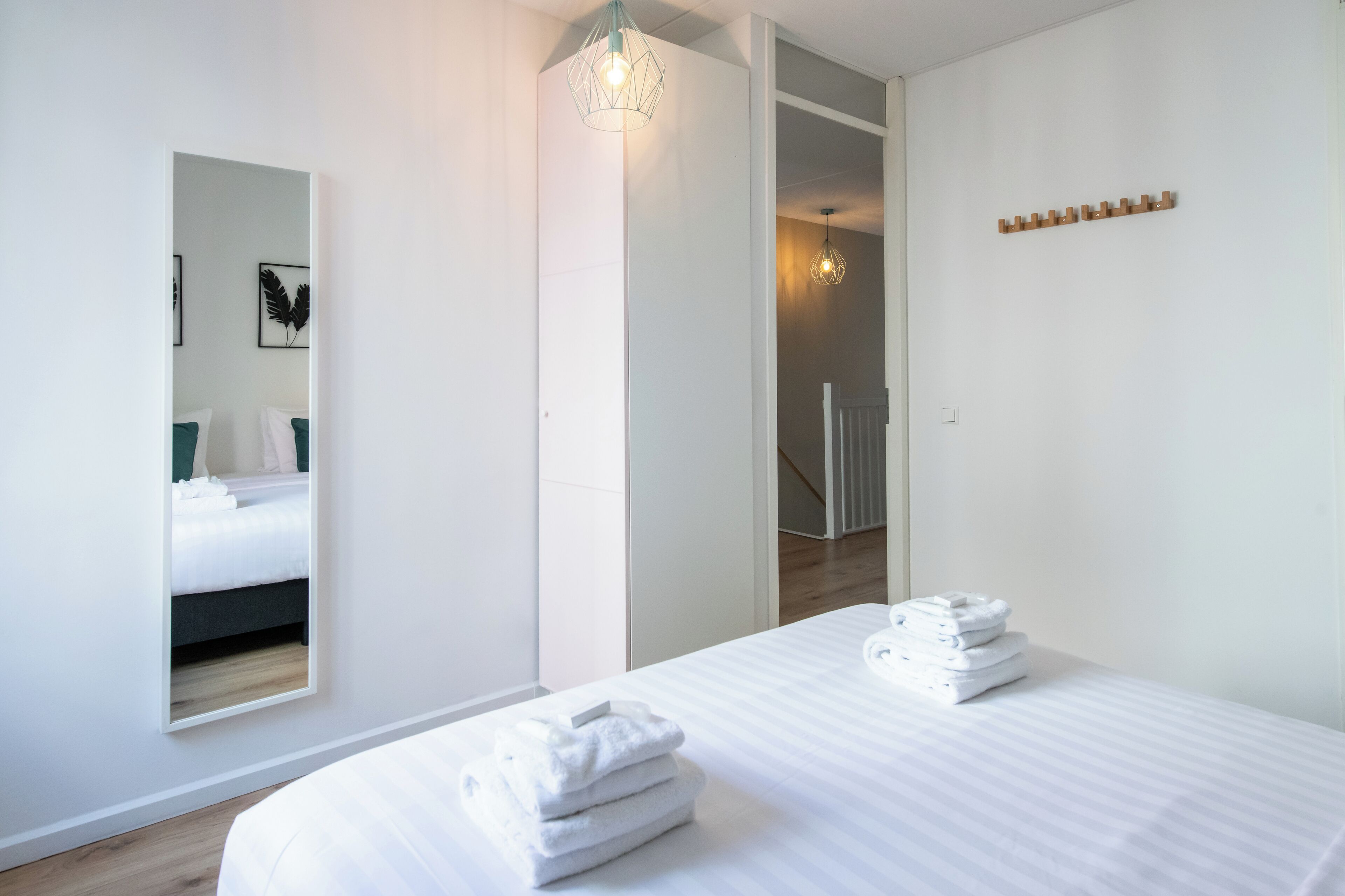 Ein modernes Hotelzimmer mit einem großen Bett, einem Spiegel und einem ordentlich gestapelten Handtuchstapel.