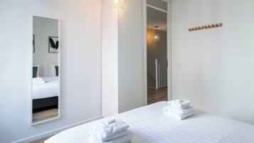 Ein modernes Hotelzimmer mit einem großen Bett, einem Spiegel und einem ordentlich gestapelten Handtuchstapel.