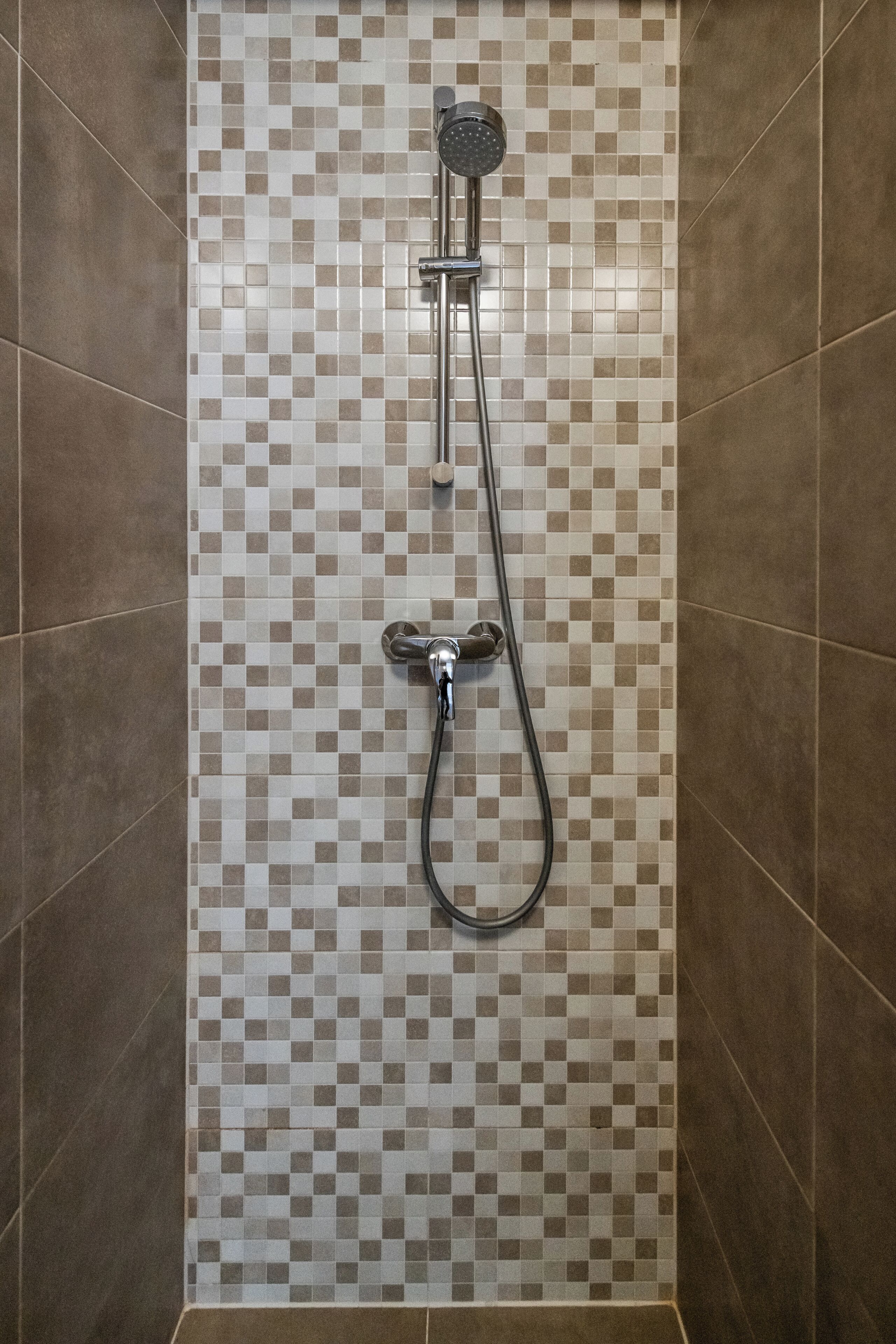 Een douche met een betegelde muur in ruitpatroon en een handdouche.