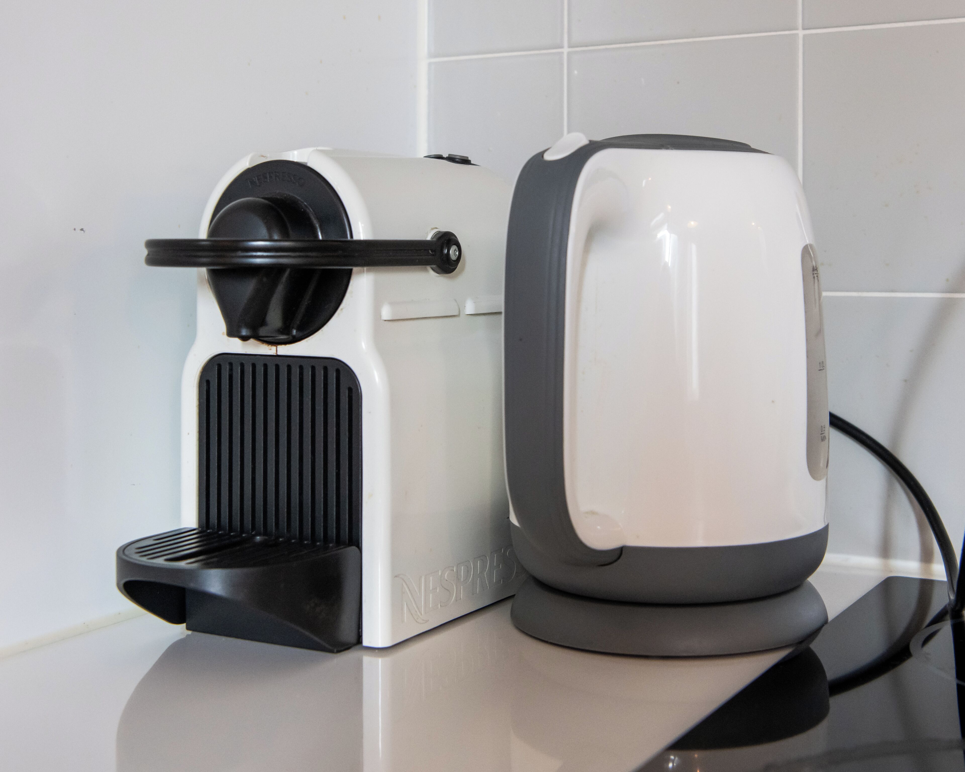Une machine à café dotée d’un bac d’égouttage noir et d’une base blanche, reliée à un câble d’alimentation.