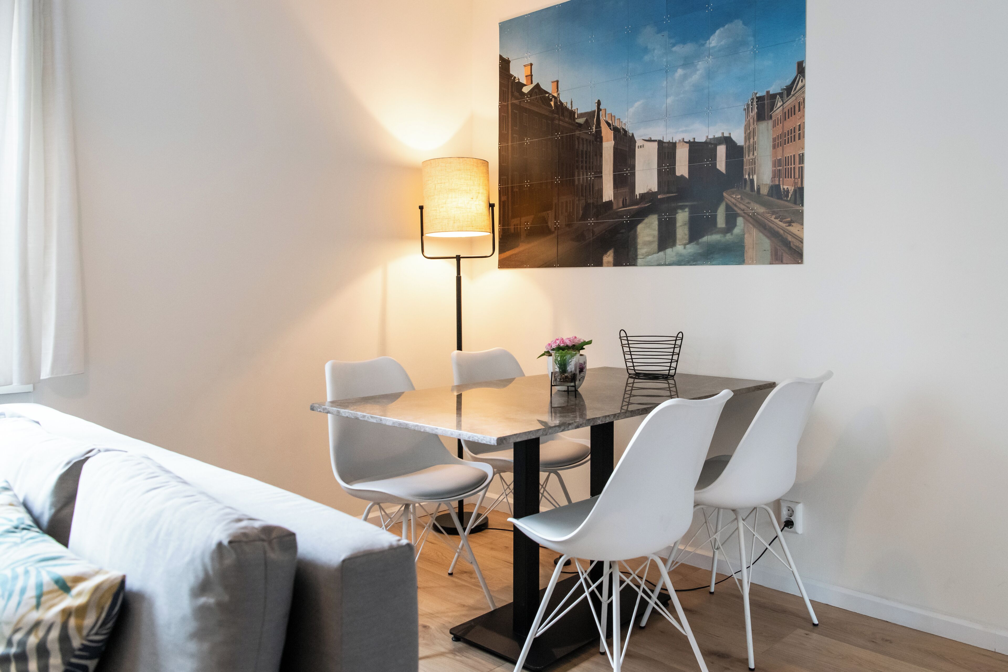 Ein modernes Zimmer mit einem Esstisch, weißen Stühlen, einer Stehlampe und einem Stadtbild.