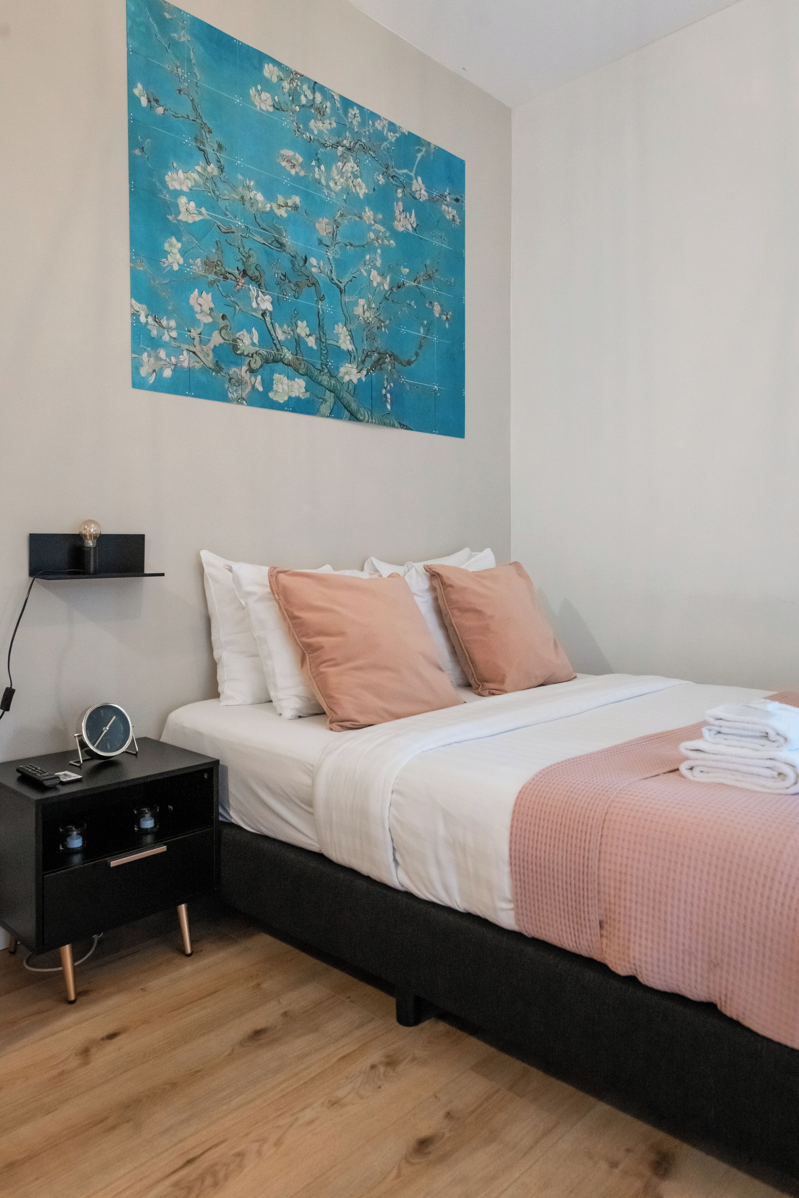Une chambre à coucher comprenant un lit, une table de chevet, une étagère fixée au mur et un grand tableau.