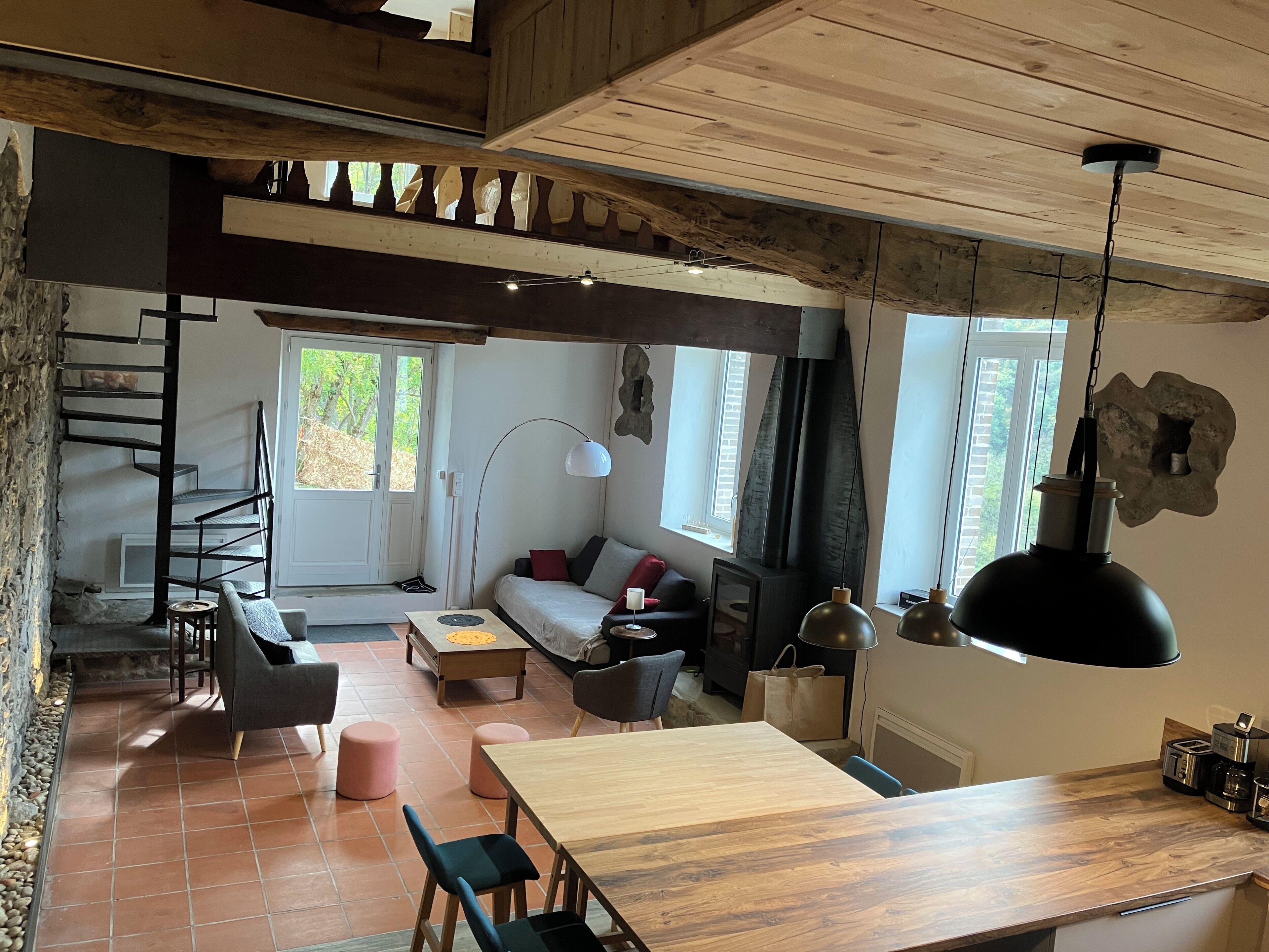 Een gezellig interieur met een houten plafond, een spiltrap, een bank, een eettafel en een keuken met een koffieapparaat.