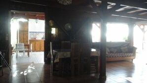 Un'ampia zona giorno con un tavolo da pranzo in legno, un divano e una poltrona. È presente un'ampia finestra che fa entrare luce naturale, e si può vedere una ventola a soffitto.