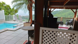 Area piscina con tavolo e sedie, vista sul verde circostante e zona relax coperta.