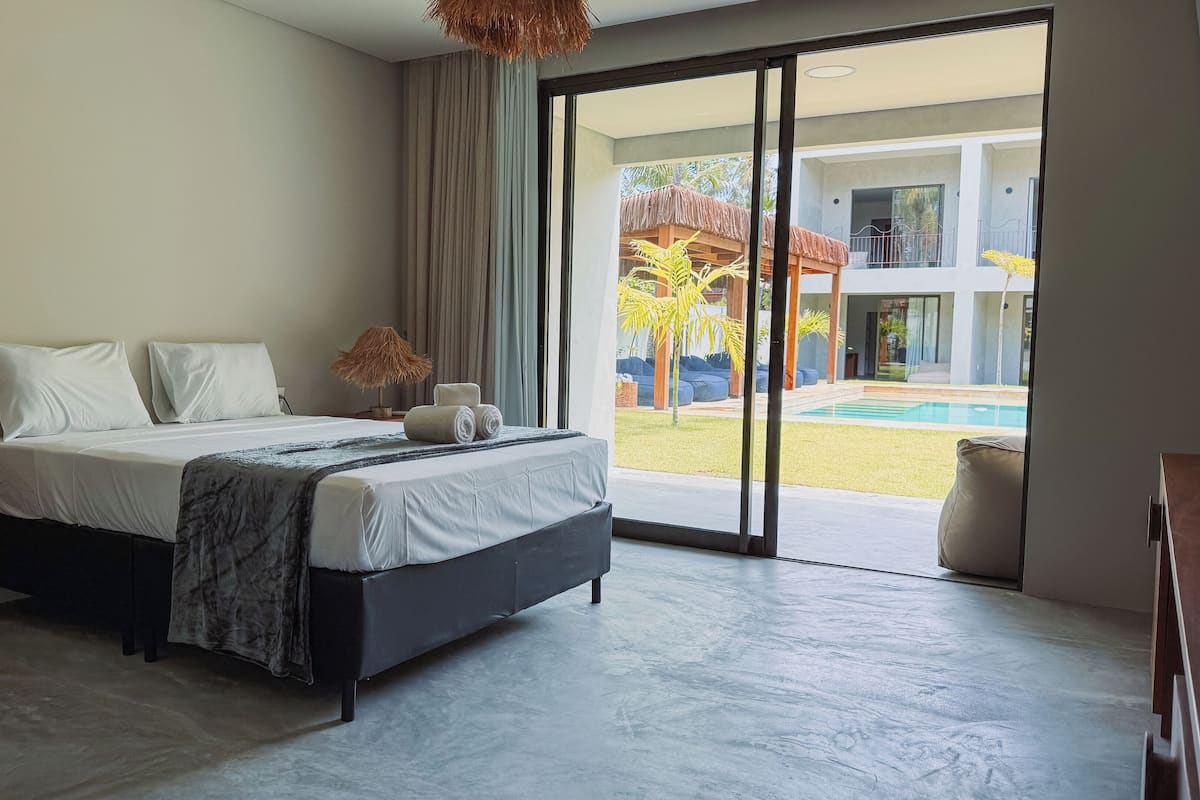 A modern hotel room with a large bed, a view of a swimming pool, and a balcony.