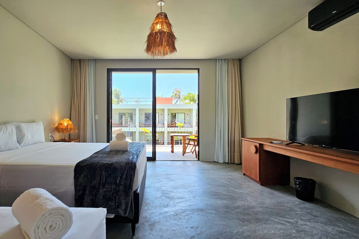 A hotel room with a bed, a desk with a TV, a lamp, and a view of the outside balcony.