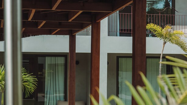 Een overdekt buitengebied met een houten plafond, een balkon met een hekwerk en een potplant.