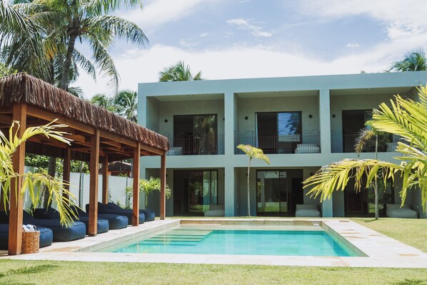 Una casa moderna de dos pisos con piscina, zona de estar cubierta y exuberante vegetación tropical.
