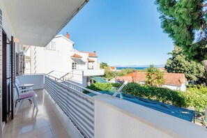 A balcony with a table and chairs, overlooking a coastal area with houses and greenery. - Apartment Mia (Supetar)