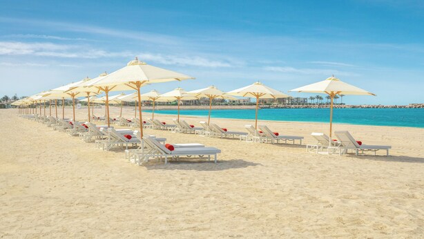 A beach with rows of white sun loungers and beige umbrellas.