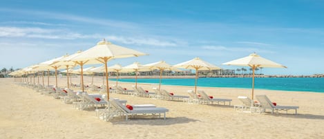 A beach with rows of white sun loungers and beige umbrellas.