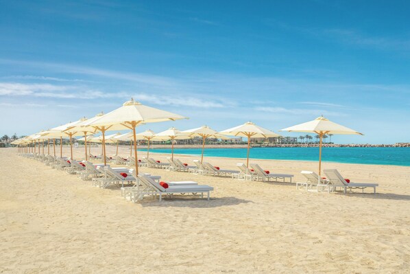 Una playa con hileras de tumbonas blancas y sombrillas color beige.