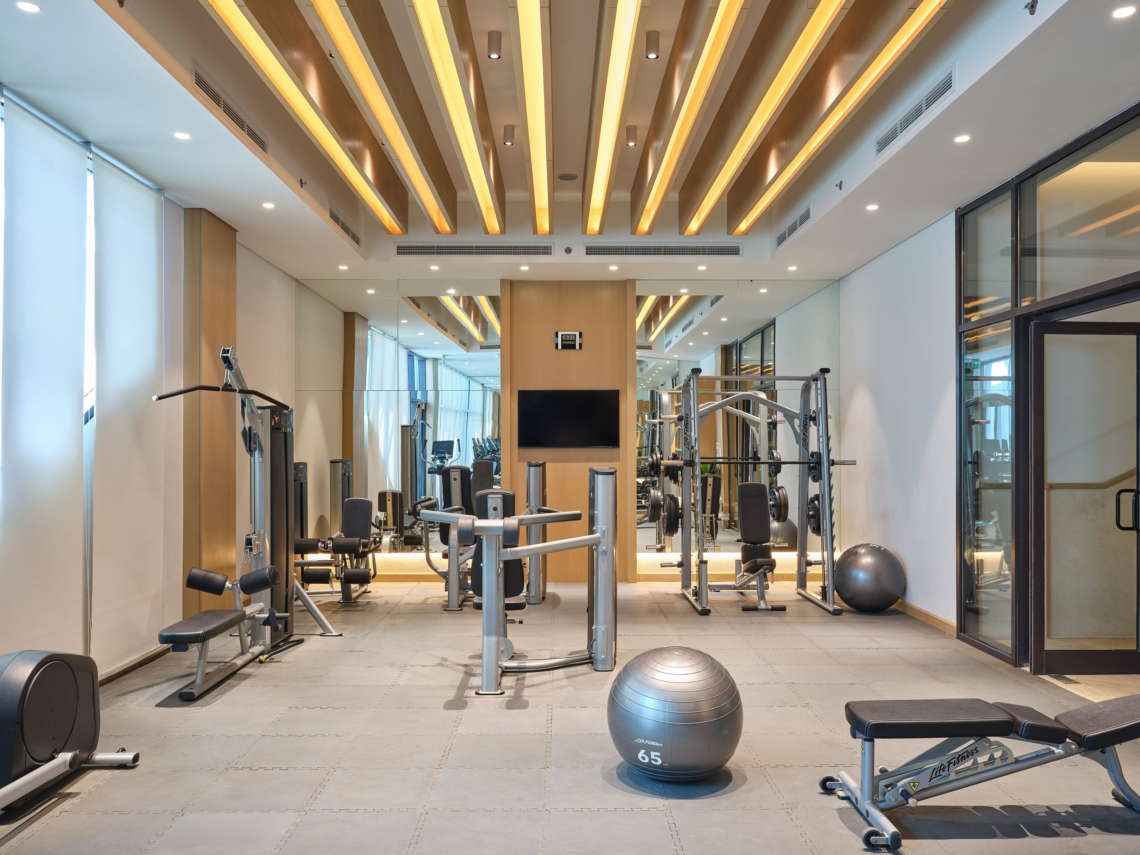 A gym with various exercise equipment, a large exercise ball, and a television screen on the wall.