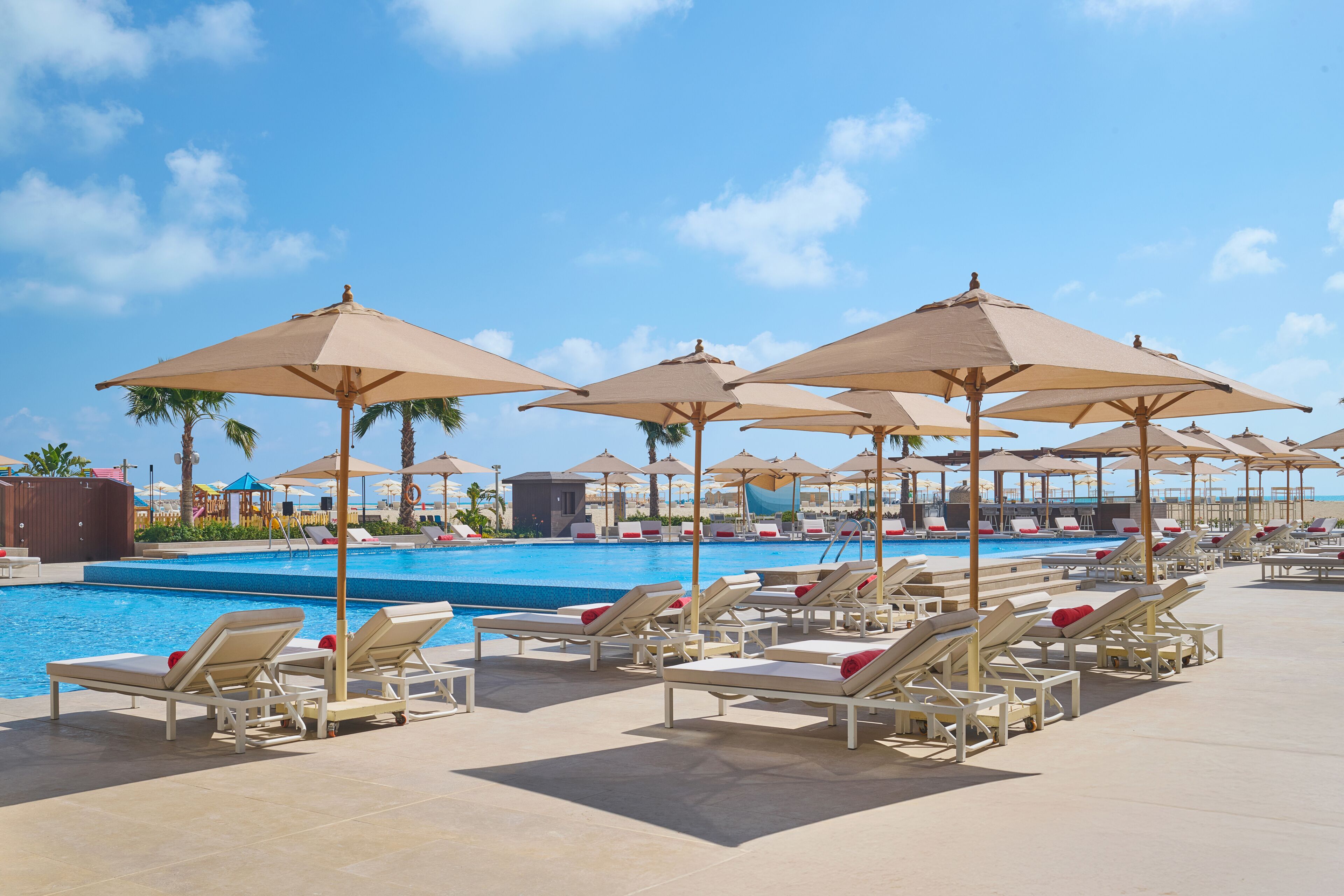 A poolside area with sun loungers and umbrellas, a clear sky, and a pool.