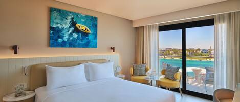 A hotel room with a large bed, a painting, a view of the sea, and a balcony with chairs.
