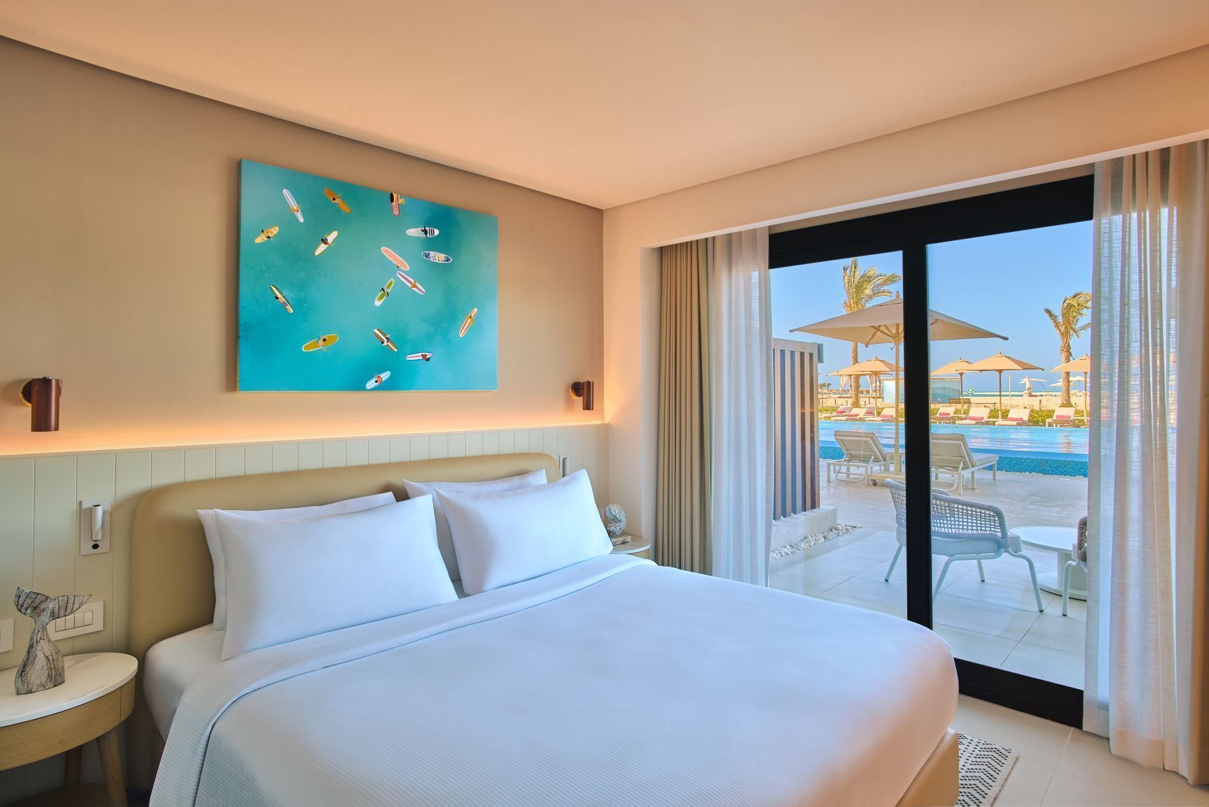 Habitación de hotel con cama, un cuadro, vista a una piscina y sillas de descanso.