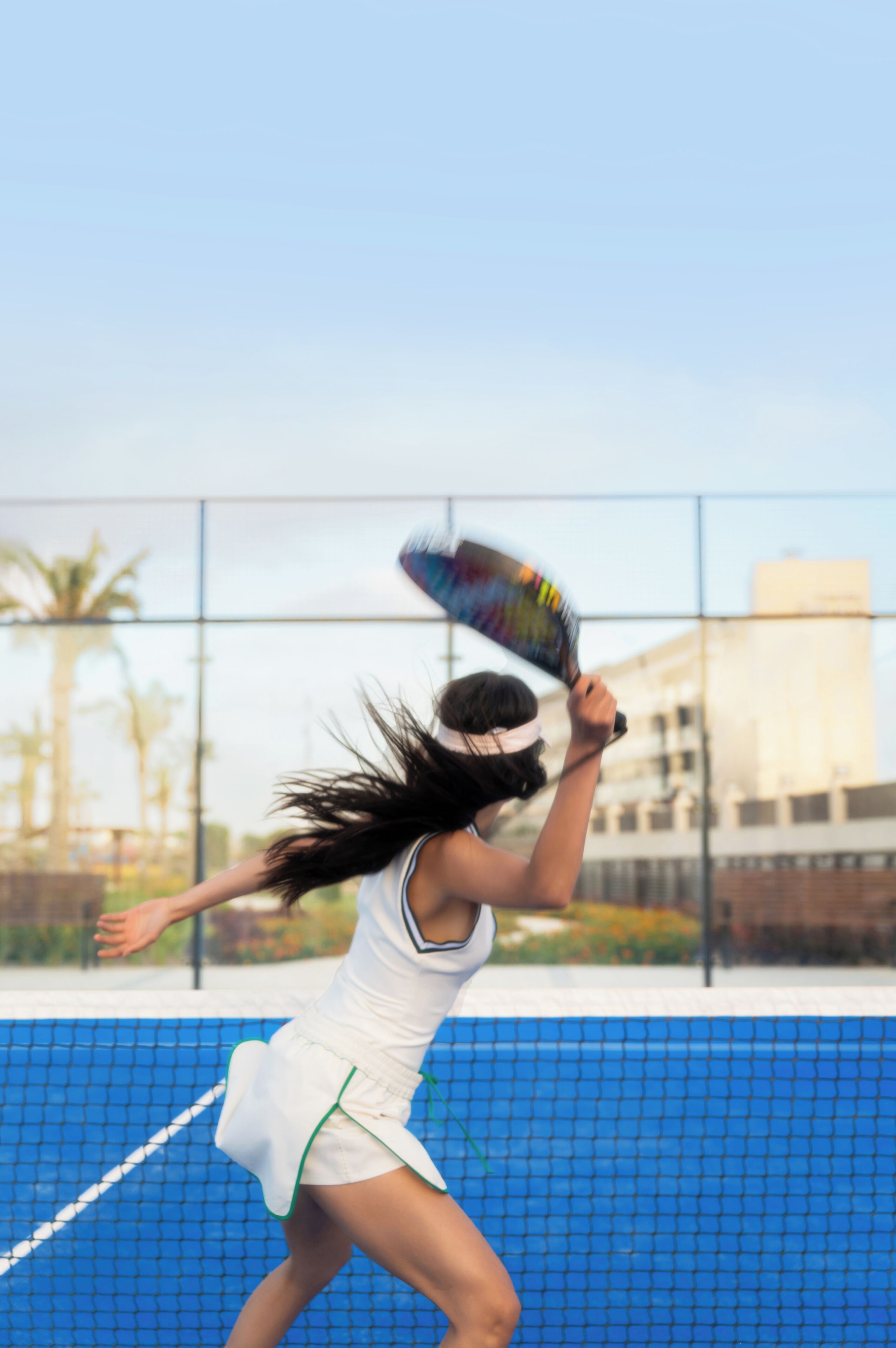 A tennis player in motion on a court with a net barrier and a building in the background.