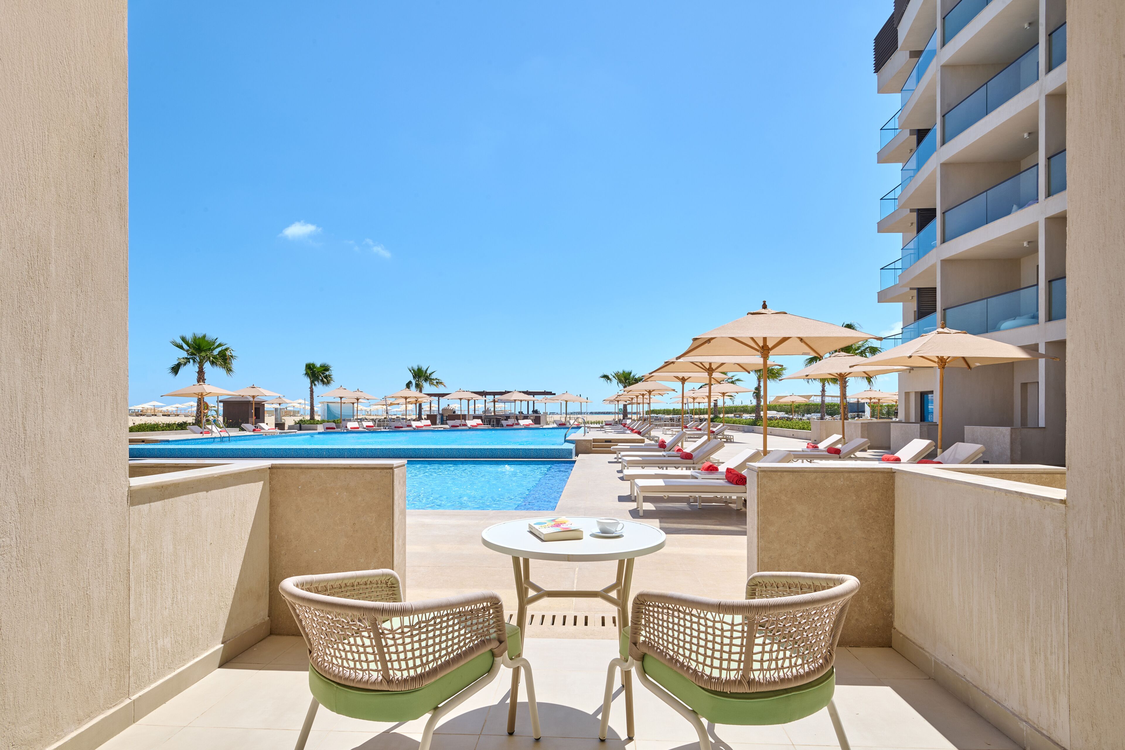A poolside area with lounge chairs and umbrellas, a pool, and a view of the ocean.