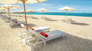 A beach with rows of white sun loungers and beige umbrellas.