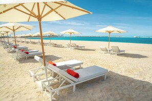 Una playa con filas de tumbonas blancas y sombrillas color beige.