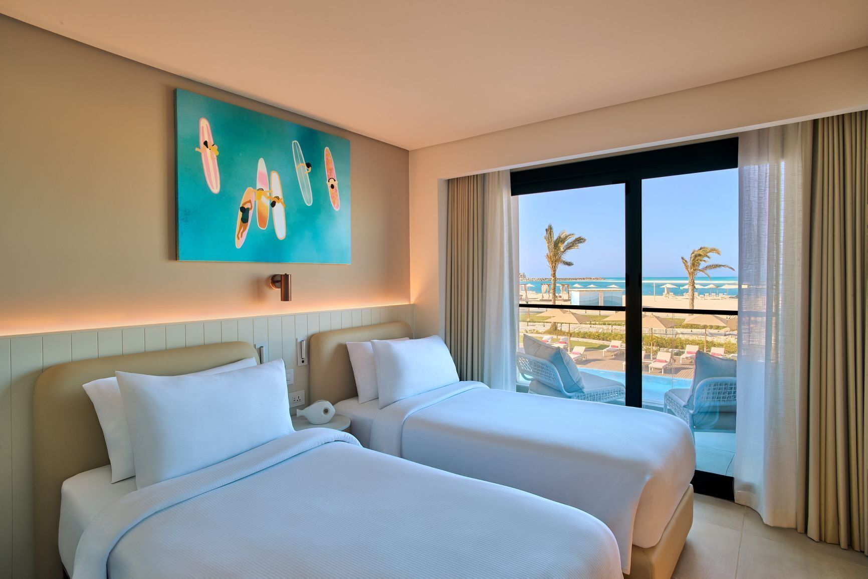 A hotel room with two beds, a large window with a view of the beach, and a painting on the wall.