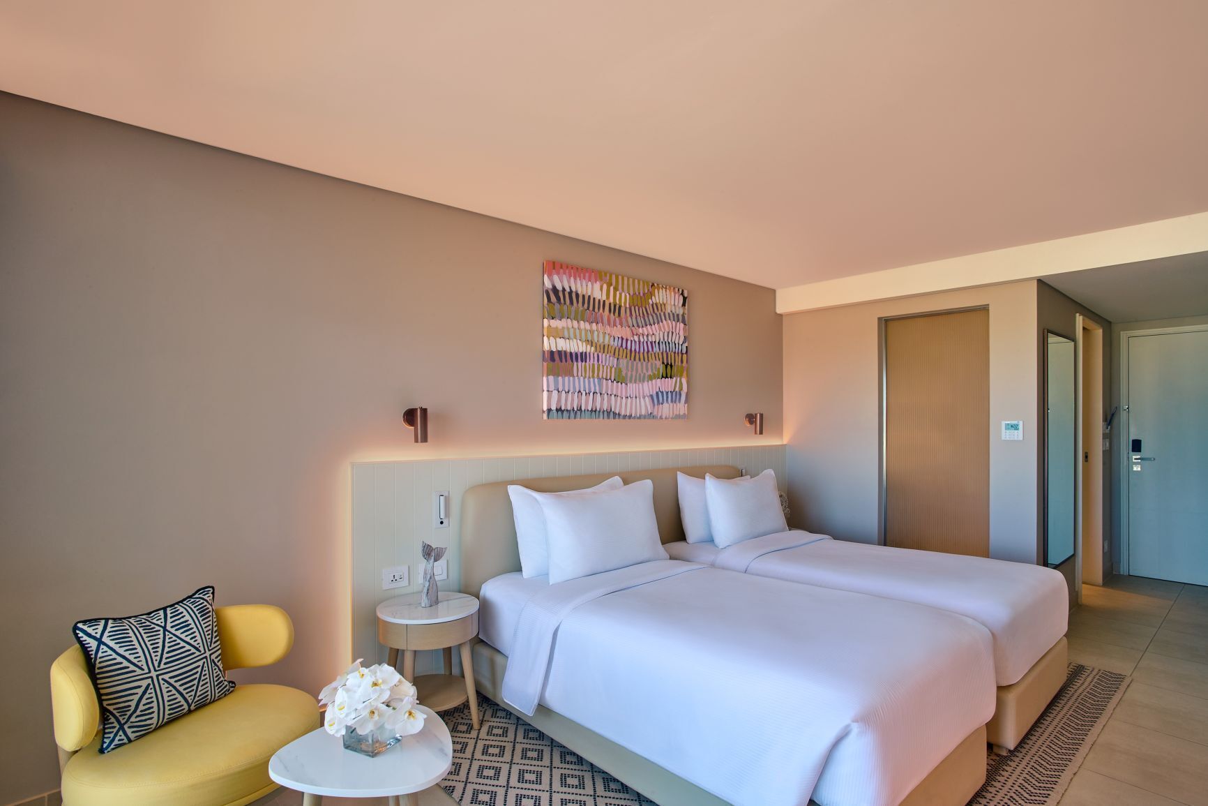 A hotel room with a bed, a chair, a small table, and a decorative wall piece.