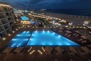 Un resort con una gran piscina, zonas de descanso en la playa y vistas al océano.