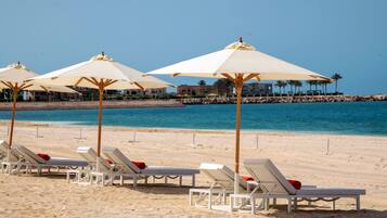 En privat strand, hvidt sand, liggestole, parasoller