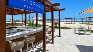 A beach bar named "Whispers Beach Bar" with a bar counter, seating, and a view of the beach.